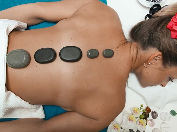 warme Steine auf dem Rücken einer Klientin bei der Hot-Stone-Massage